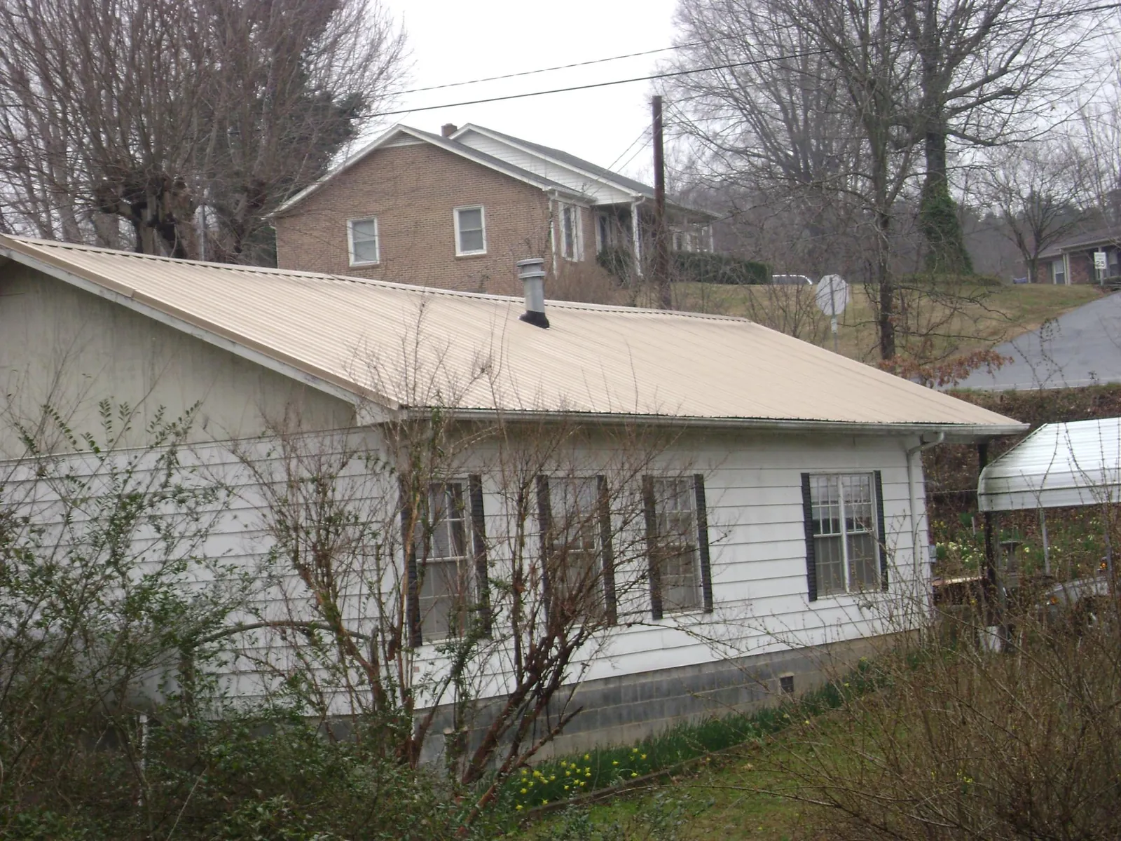 Tan metal roof on a white sided house set into a hillside — Commercial Roofing by Roofing Brothers in Camden